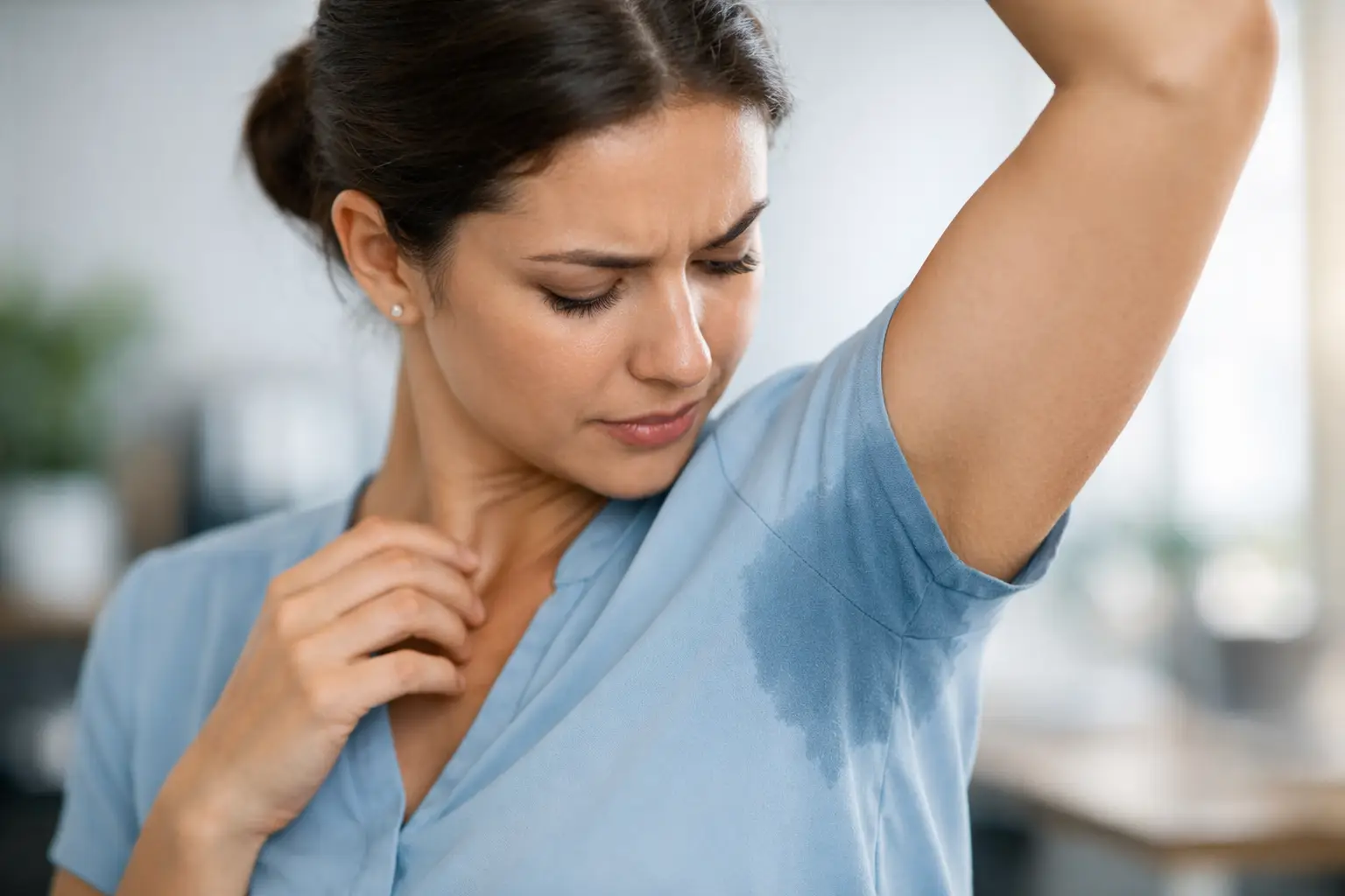 Mulher observando mancha de suor excessivo na axila da camisa azul